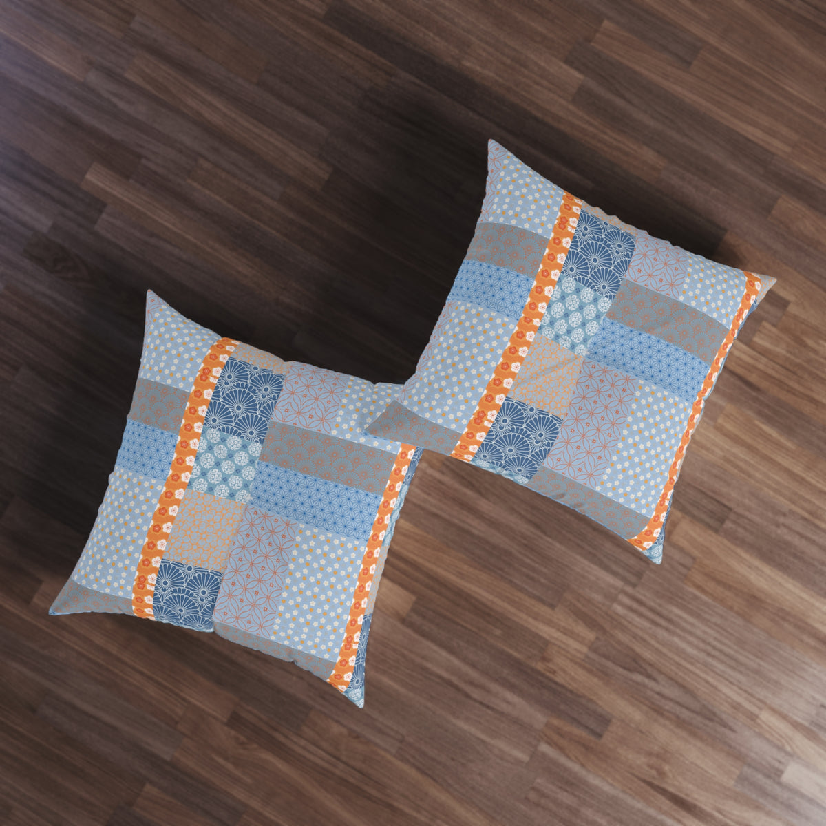 Two square throw pillows with a blue, gray, and orange patchwork pattern, displayed on a dark wood floor.