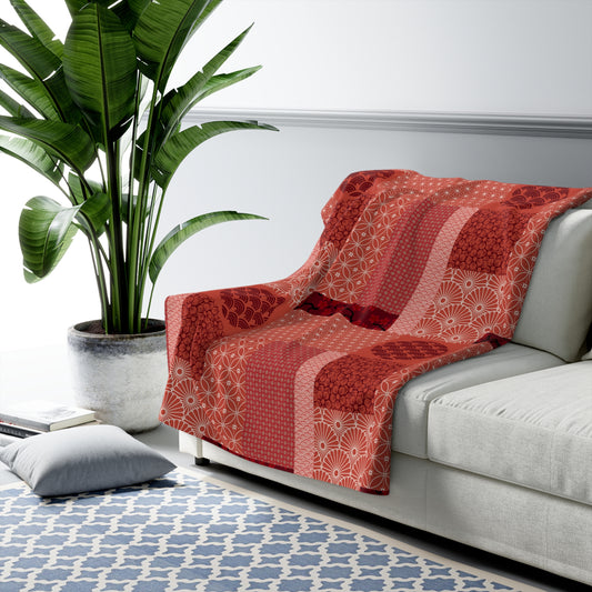 Red patterned throw blanket on a gray sofa with a plant and rug in the background