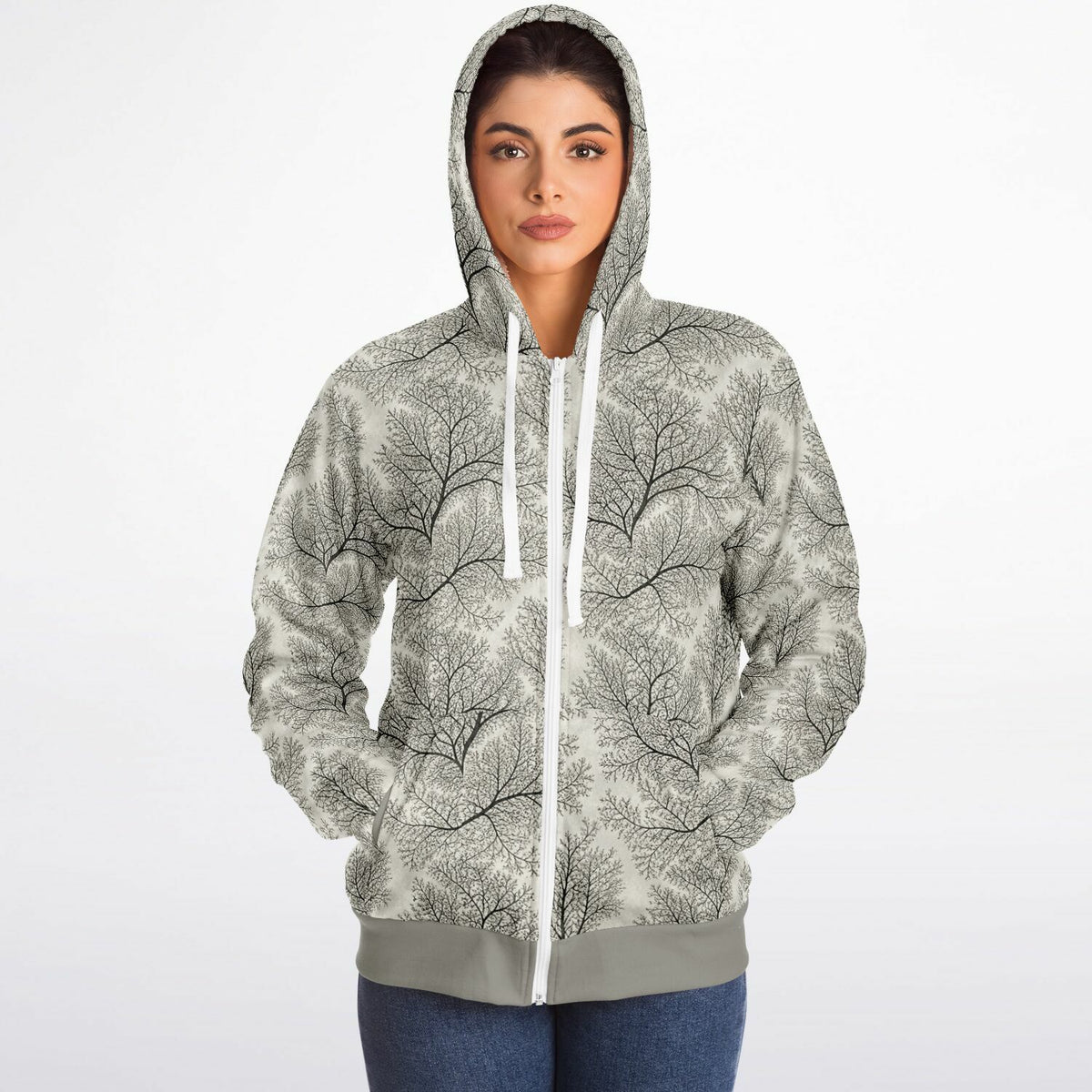 A woman wearing a light gray zip-up hoodie with a black tree branch pattern and white drawstrings, paired with blue jeans, against a plain white background.