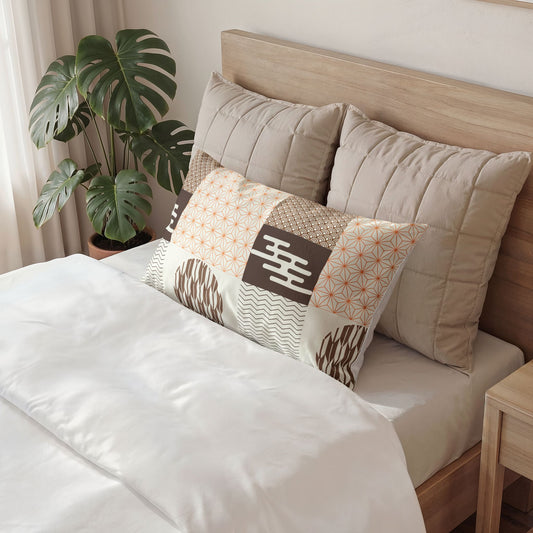 A styled bedroom scene showing a bed with white bedding, large beige pillows, and a decorative rectangular accent pillow with patchwork patterns in beige, brown, white, and orange. A wooden headboard, side table, and potted monstera plant are visible.