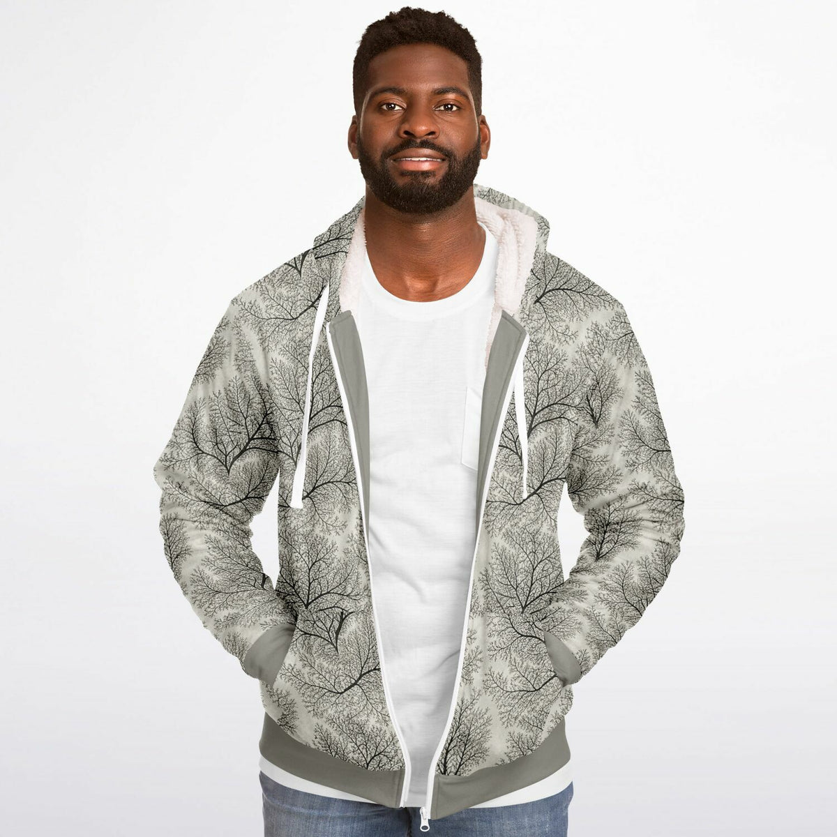 A man wearing a light gray and white zip-up hoodie with a black tree branch pattern, layered over a white t-shirt and blue jeans, against a plain white background.