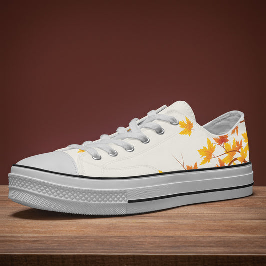 A white low-top canvas sneaker with a yellow and orange autumn leaf print on the side, resting on a wooden surface against a dark brown background.