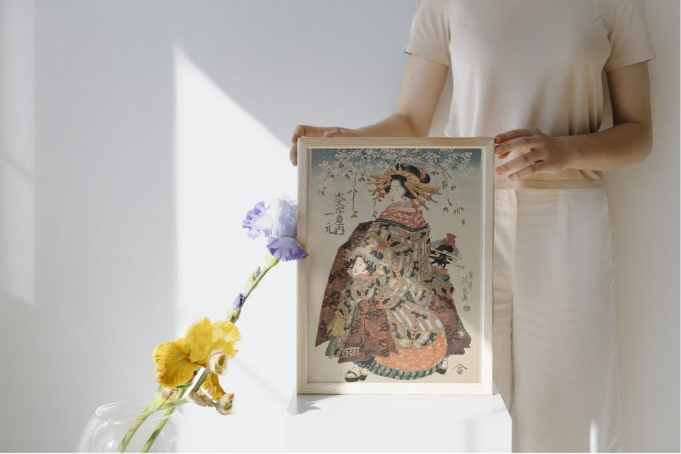 Person holding a framed artwork of a traditional dress against a white wall.