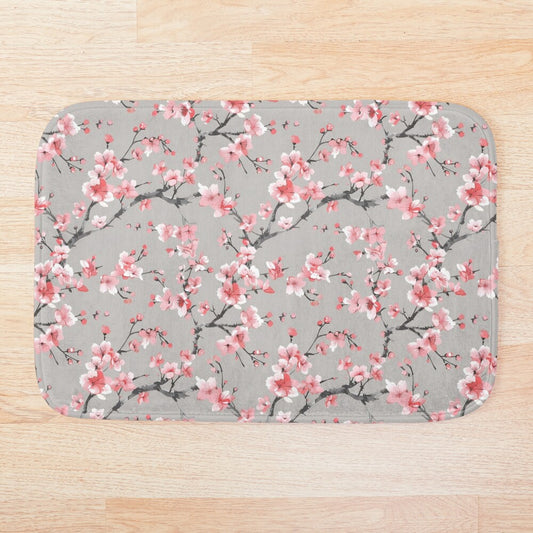 Embrace the vibrant energy of a Japanese spring with the Pink Sakura Bath Mat. This eye-catching bathmat features a cheerful pattern of stylized blossoms reminiscent of delicate cherry blossoms (sakura), rendered in shades of white against a soft grey background
