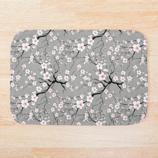 This eye-catching bathmat features a cheerful pattern of white stylized blossoms reminiscent of delicate cherry blossoms (sakura), rendered in shades of white against a soft grey background