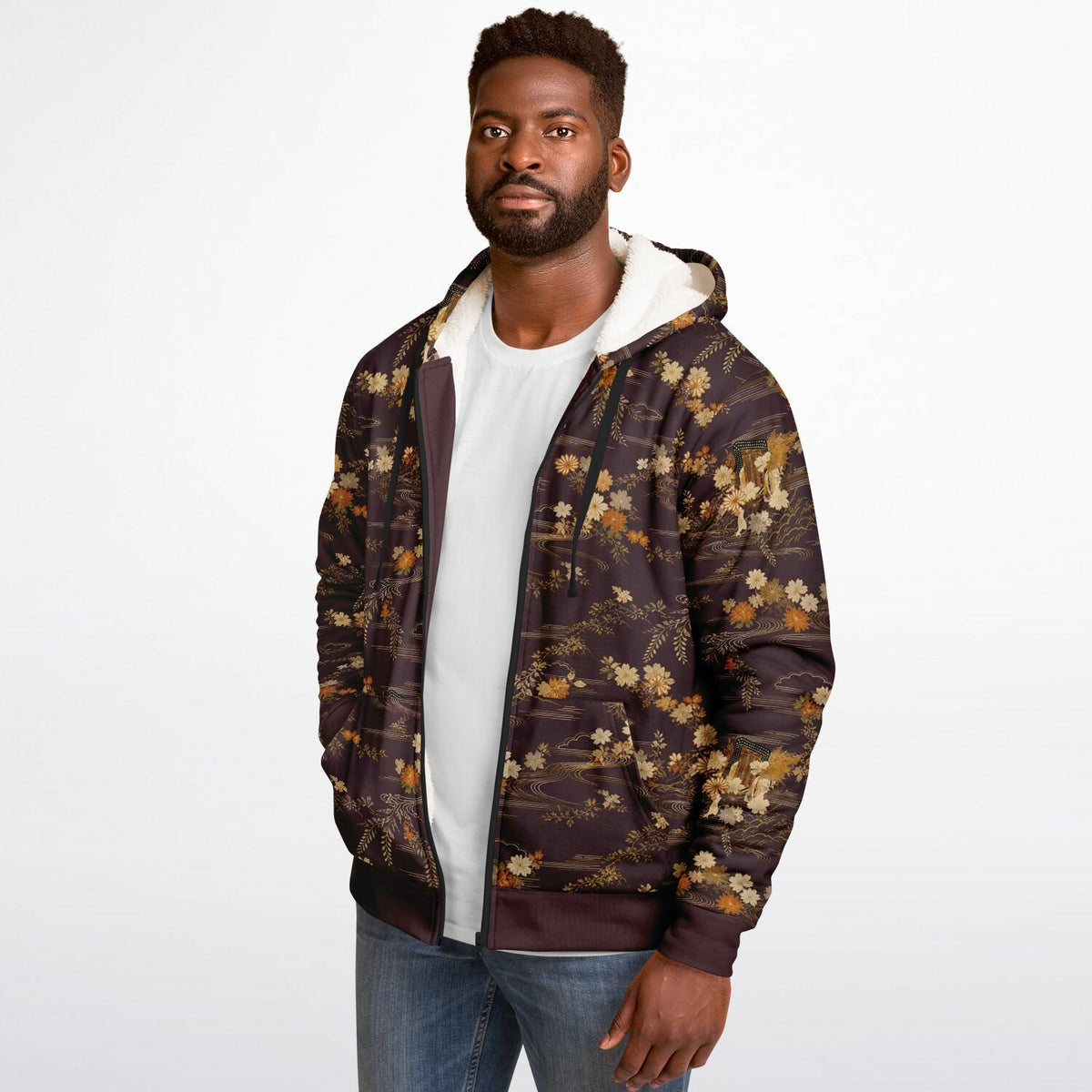 A man wearing a dark brown and black floral patterned zip-up hoodie with a white hood lining, layered over a white t-shirt and blue jeans, against a plain white studio background.