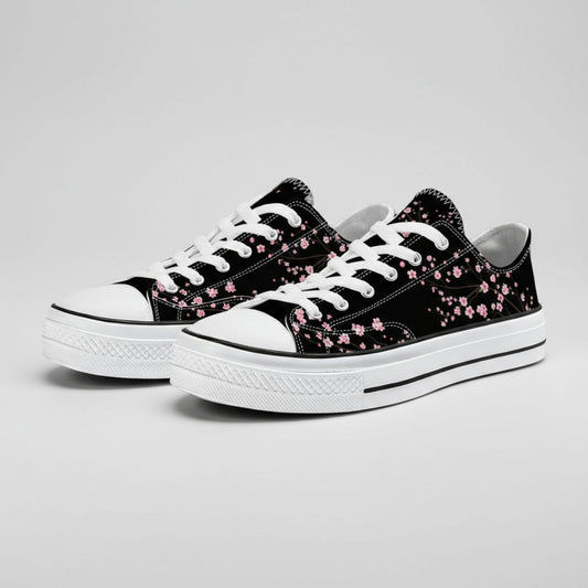 Classic black low-top canvas sneakers featuring an elegant pink cherry blossom (Sakura) pattern, photographed on a cobblestone surface.