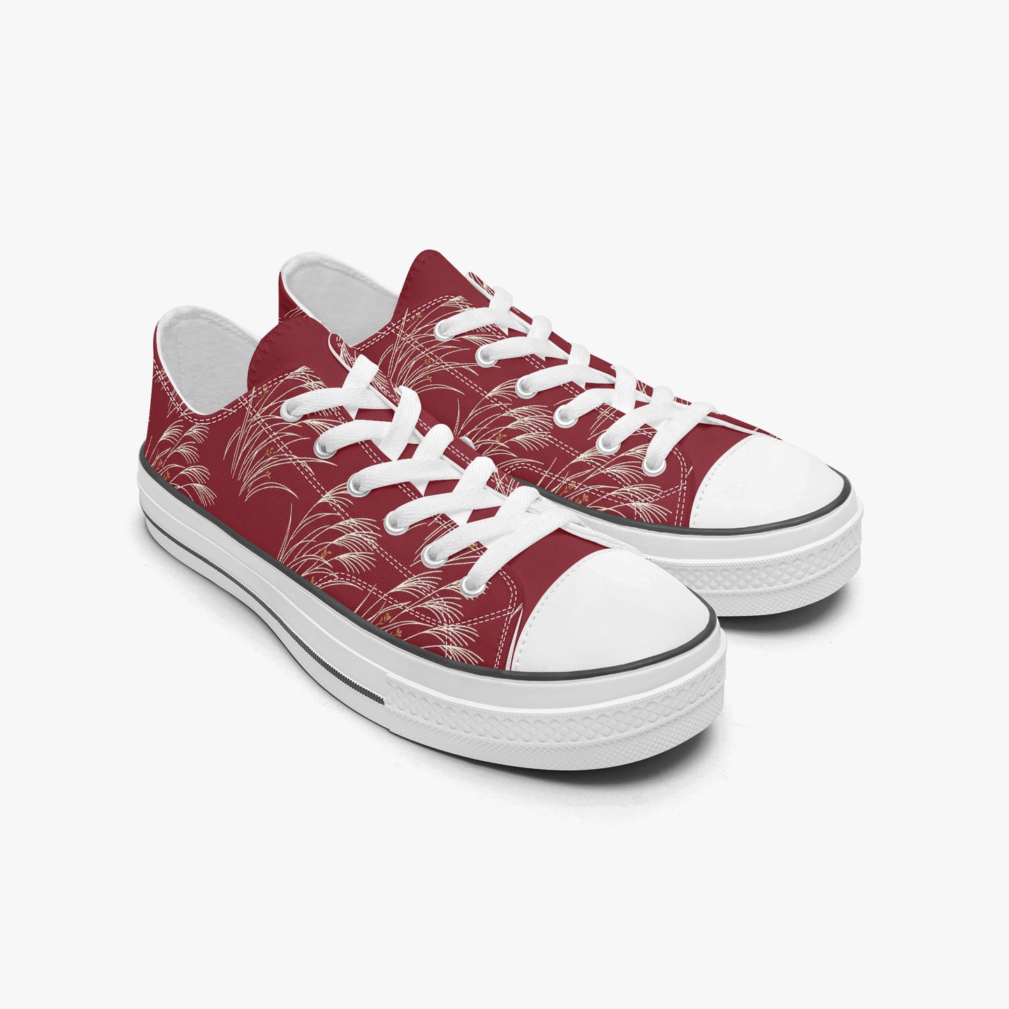 A pair of low-top canvas sneakers in burgundy red with a white palm leaf pattern, white laces, and white rubber toe caps and soles, shown on a light gray background.