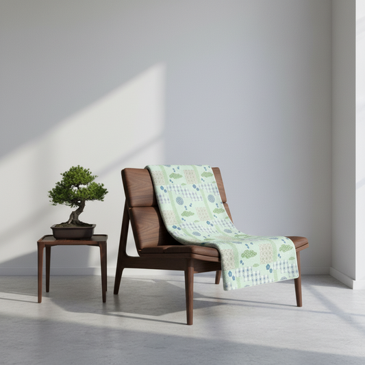 Wooden chair with a green patterned towel draped over it, next to a small table with a bonsai tree in a minimalistic room.