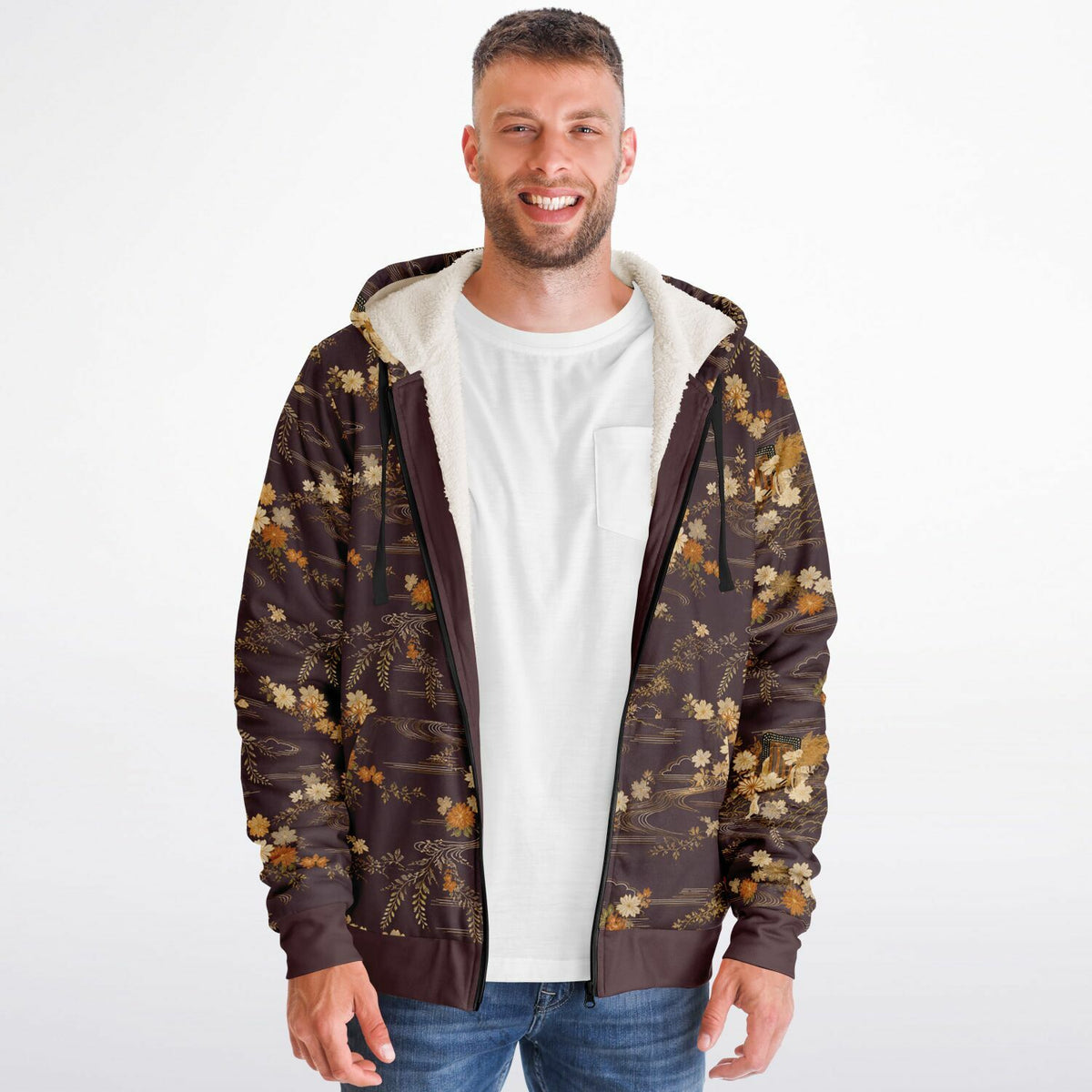 A man wearing a brown zip-up hoodie with a gold floral pattern and a white sherpa-lined hood, layered over a white t-shirt and blue jeans, against a plain white background.