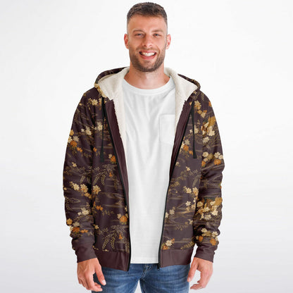 A man wearing a brown zip-up hoodie with a gold floral pattern and a white sherpa-lined hood, layered over a white t-shirt and blue jeans, against a plain white background.