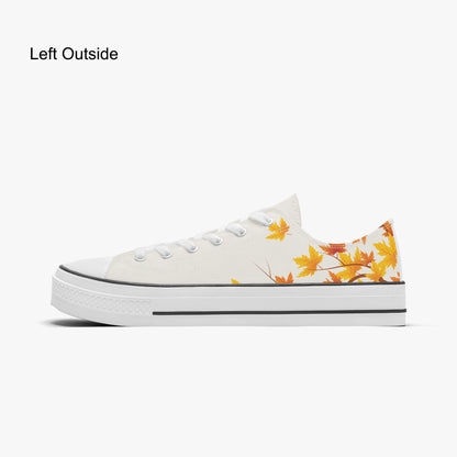 A low-top canvas sneaker shown in side profile on a light gray background. The shoe is off-white with a white rubber sole, black piping, and a pattern of orange and yellow autumn leaves on the side and heel.