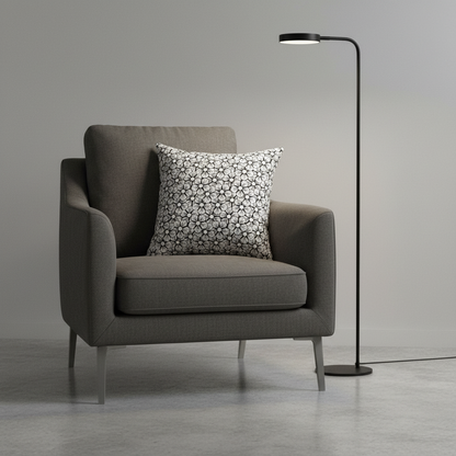 Gray armchair with a patterned pillow and a floor lamp in a minimalistic room.