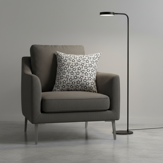 Gray armchair with a patterned pillow and a floor lamp in a minimalistic room.