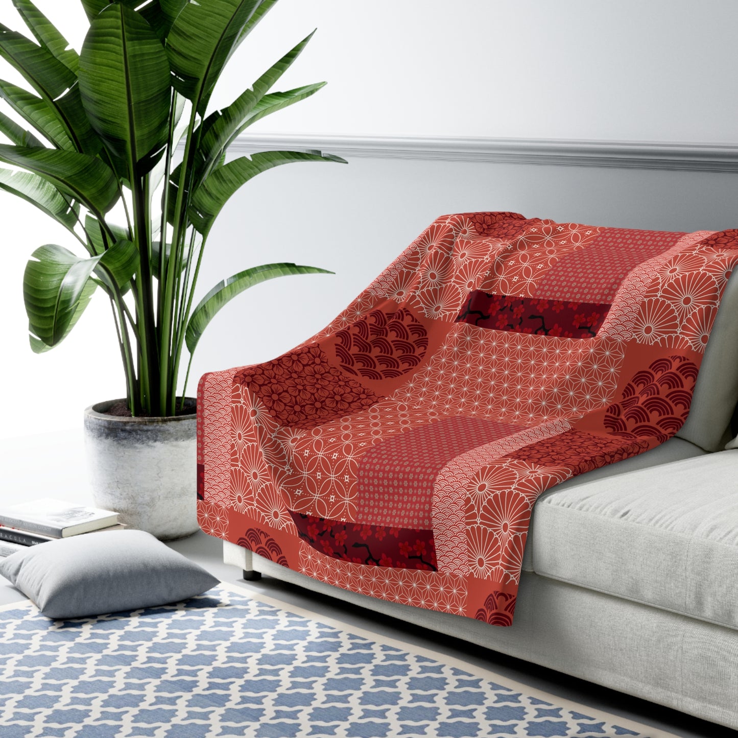 Red patterned throw blanket draped over a gray sofa in a living room with a plant and rug.