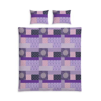A bedding set featuring a patchwork quilt and two matching pillowcases in shades of purple, pink, and dark gray, displayed on a solid white background.