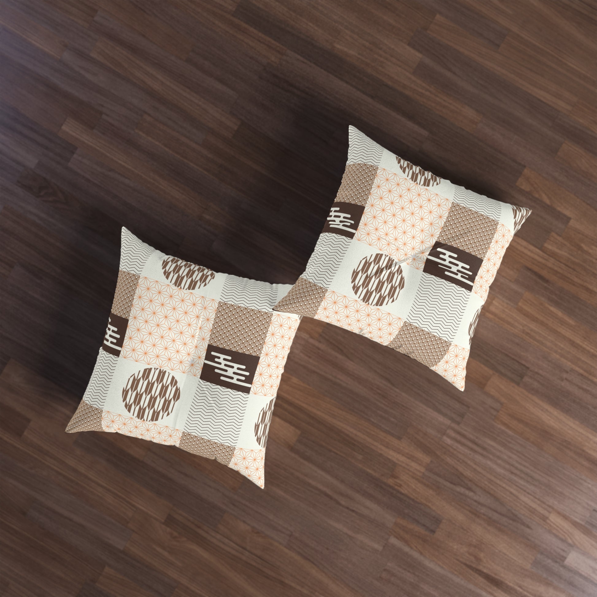Two square throw pillows with a beige, brown, and white patchwork pattern featuring geometric and dotted motifs, displayed on a dark wood floor.