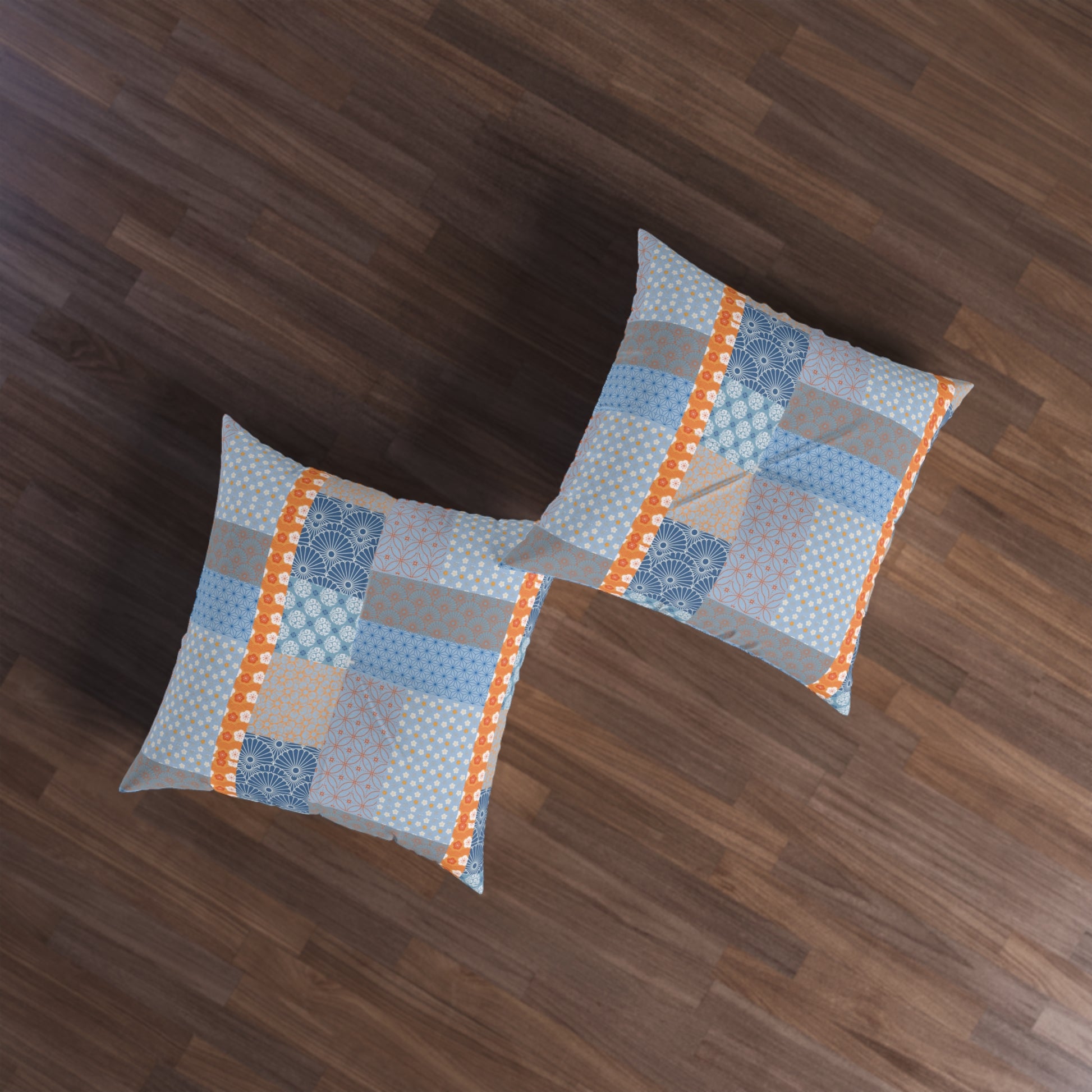 Two square throw pillows with a blue, gray, and orange patchwork pattern, displayed on a dark brown wooden floor.
