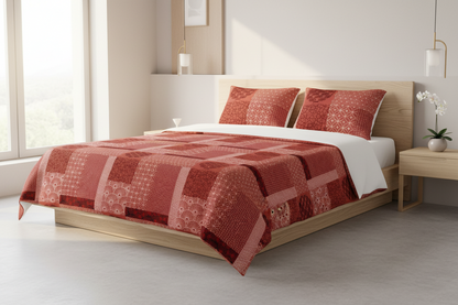 A bed dressed in a red and orange patchwork quilt and matching pillows, set in a modern bedroom with a light wood platform bed frame, white walls, and a window.