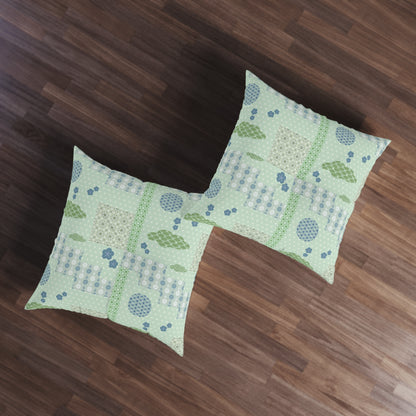 Two square decorative throw pillows with a light green and blue patchwork quilted pattern, displayed on a dark brown wooden floor.
