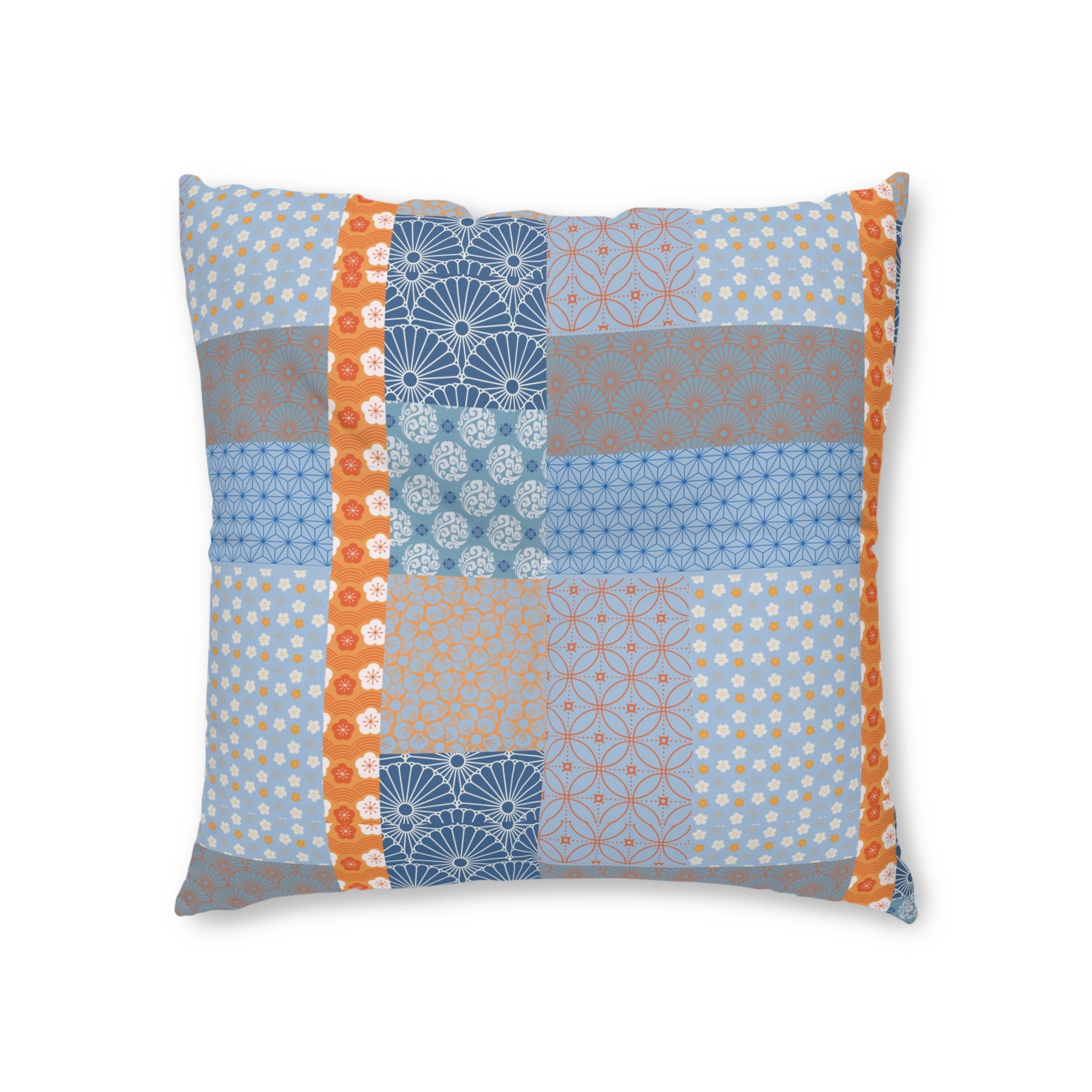 A square decorative throw pillow featuring a patchwork design of various blue, gray, and orange patterns, framed by orange vertical borders on the left and right, set against a plain white background.