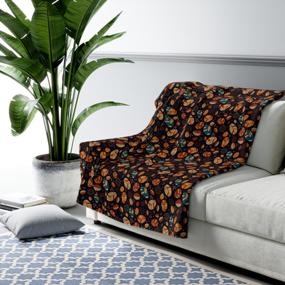 A dark throw blanket with an orange, brown, and teal leaf pattern draped over a light gray sofa in a modern living room setting with a potted plant and patterned rug.