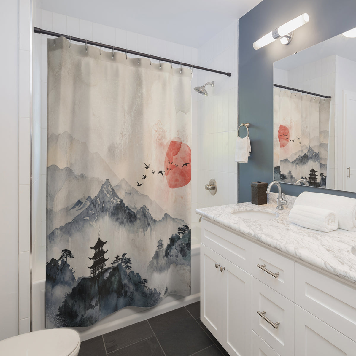 A bathroom scene showing a shower curtain with a Japanese-inspired landscape print featuring misty mountains, a pagoda, birds, and a red sun. The curtain is hanging in a modern bathroom with white cabinetry, a marble countertop, a mirror, and a blue-gray accent wall.