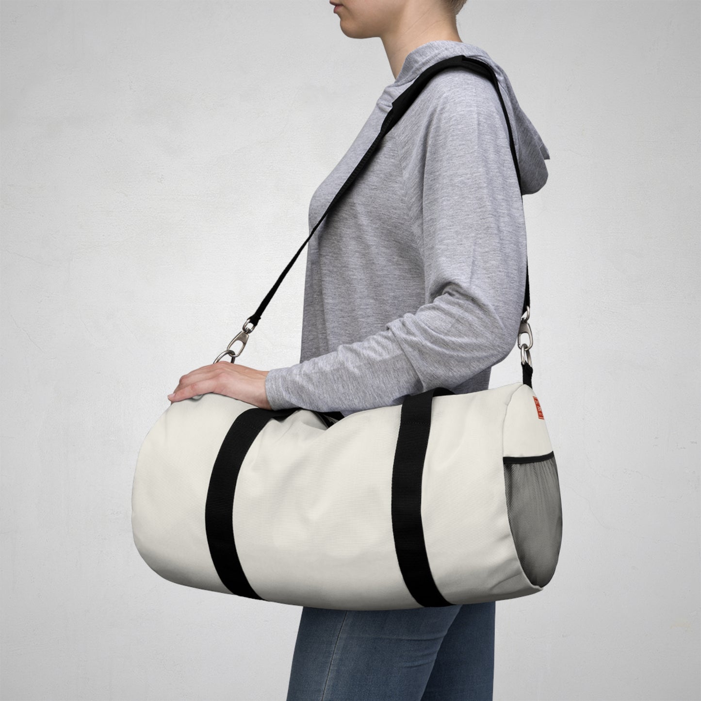 Person carrying a white duffel bag with black straps on a plain background
