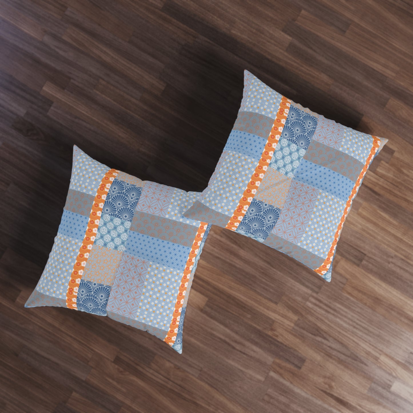 Two square throw pillows with a blue, gray, and orange patchwork pattern, displayed on a dark wood floor.