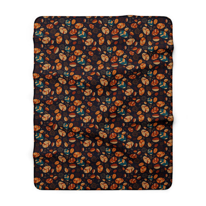 A rectangular throw blanket with a dense, all-over autumn pattern of orange and brown leaves, tan acorns, and teal birds on a very dark charcoal background, shown flat against a white background.