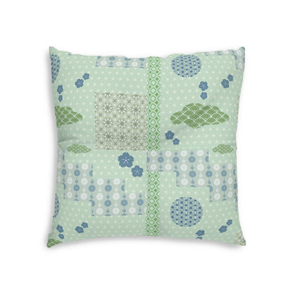A square decorative throw pillow featuring a patchwork quilted design in shades of sage green, light blue, and white, set against a plain white background.