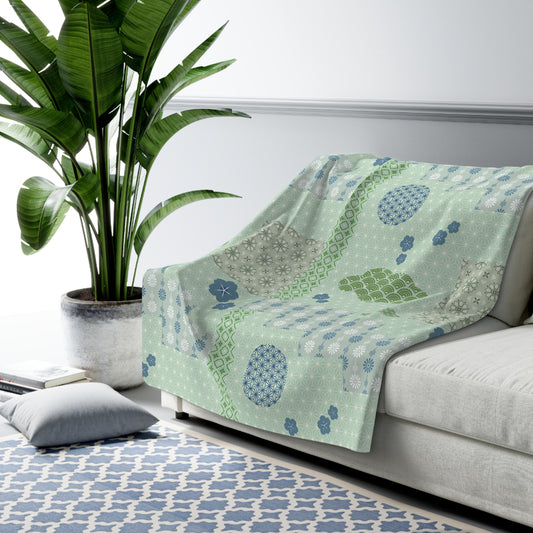 Green patterned blanket draped over a sofa in a living room with a plant and rug.