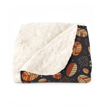 A folded throw blanket featuring a plush cream sherpa fleece backing and an autumn-themed printed fabric on the front. The print showcases orange, brown, and beige leaves on a dark navy background.