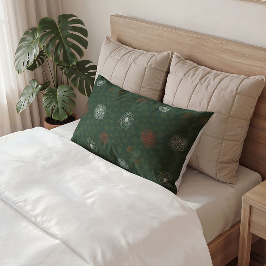 A dark green decorative lumbar pillow with a subtle floral pattern is styled on a bed with white bedding and beige pillows, next to a potted monstera plant.