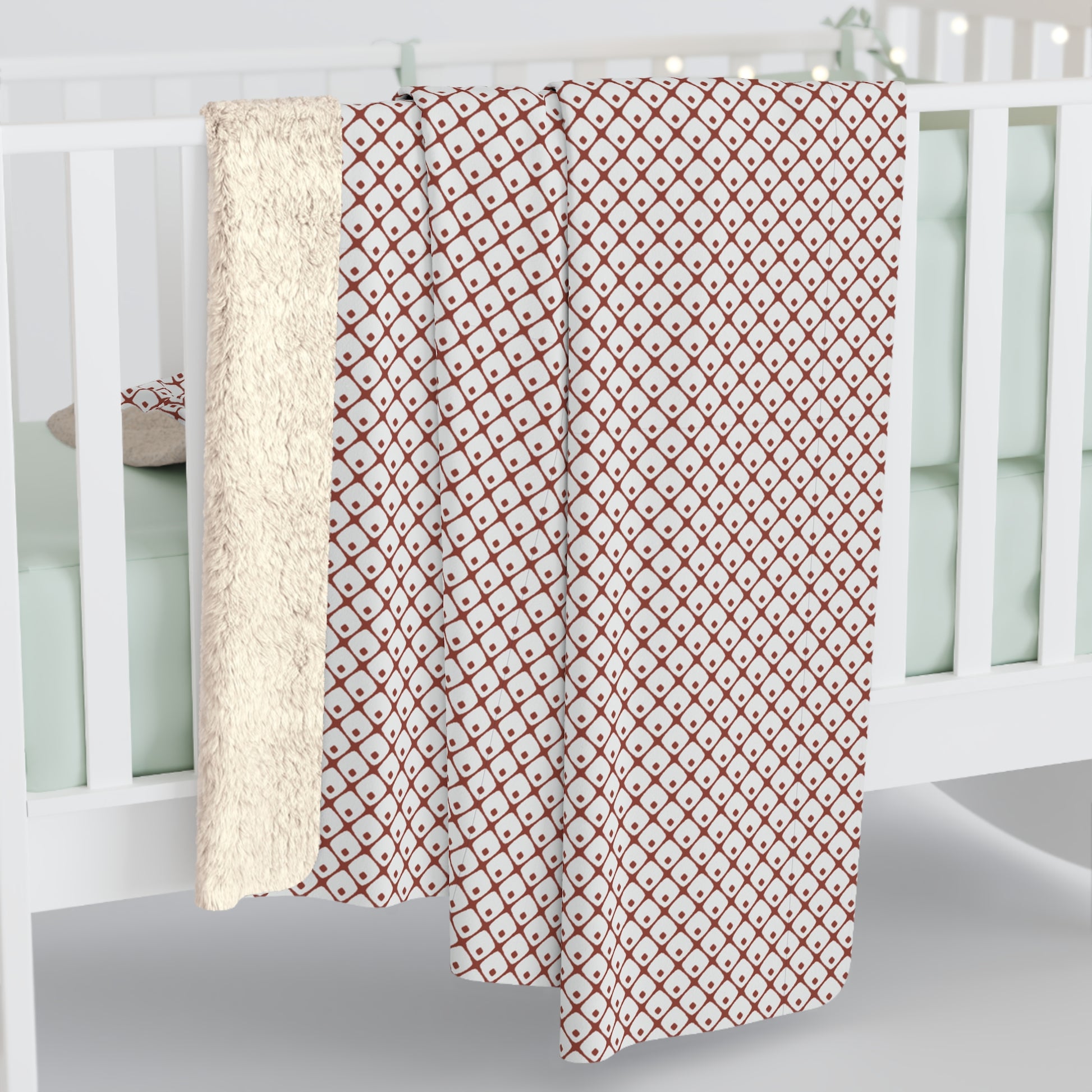Red and white patterned blanket draped over a crib with a white crib in the background.