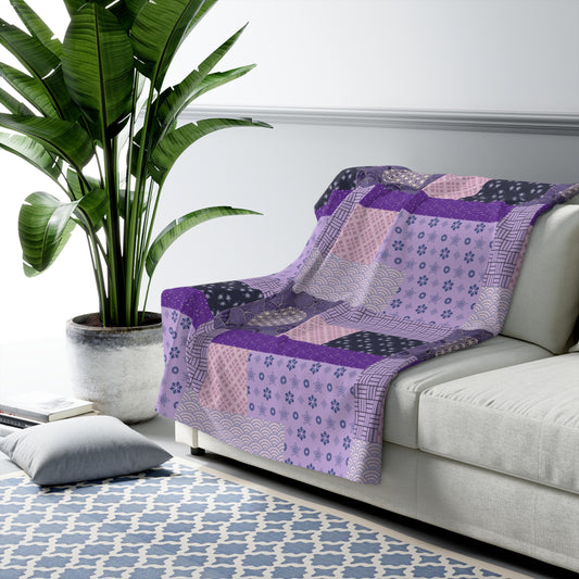 Patterned purple blanket draped over a white sofa with a plant in the background