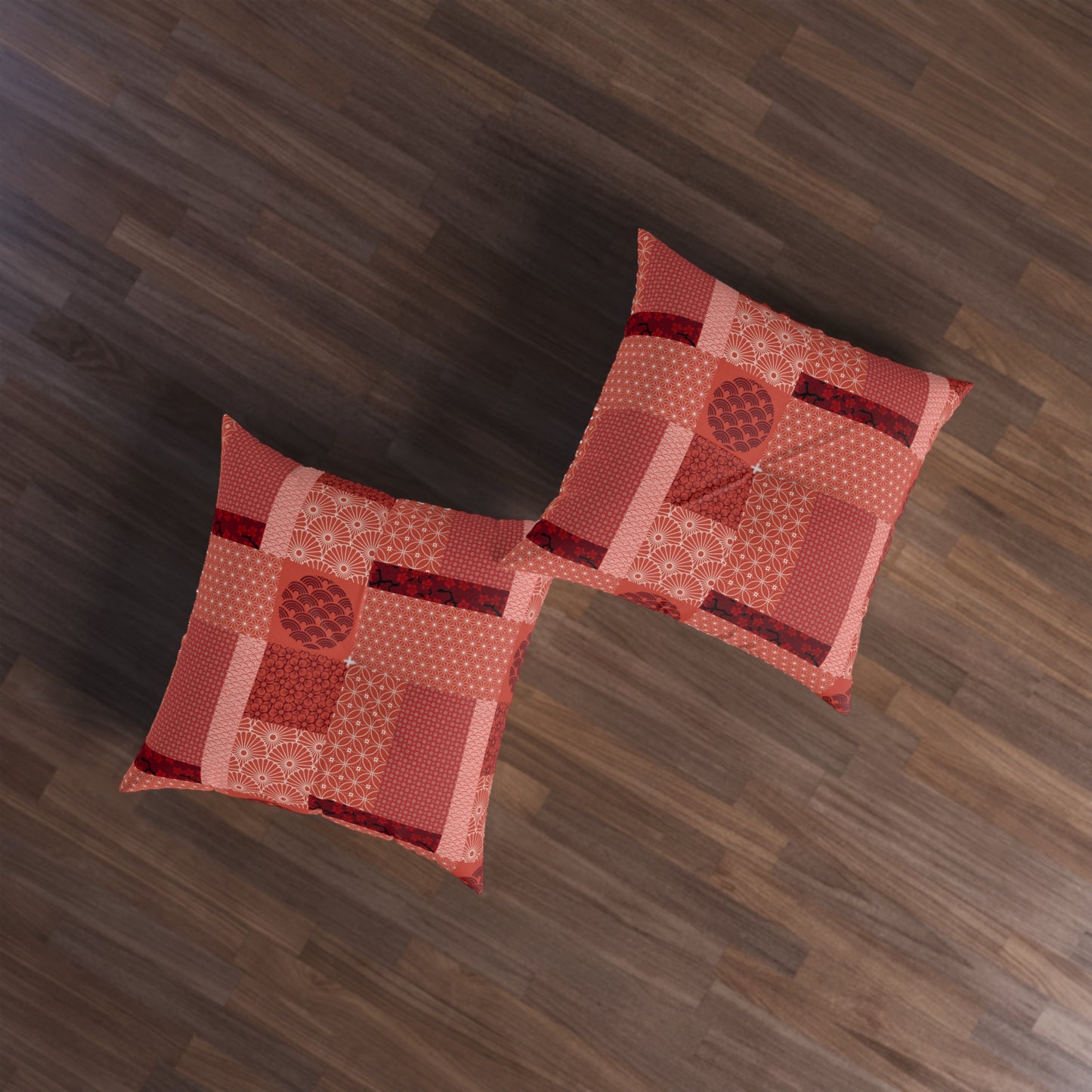Two square decorative throw pillows with a patchwork pattern in shades of red, orange, and pink, arranged on a dark brown wooden floor.