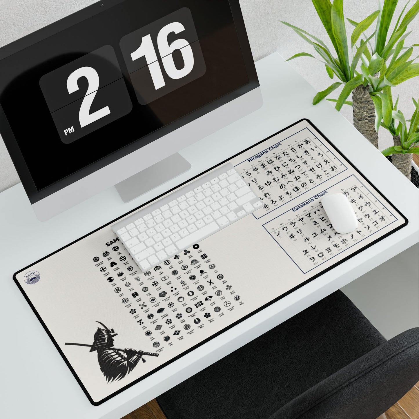 Desk setup with a large mouse pad featuring Japanese text and symbols, a computer monitor displaying '2 PM' and '16', and a plant in the background.