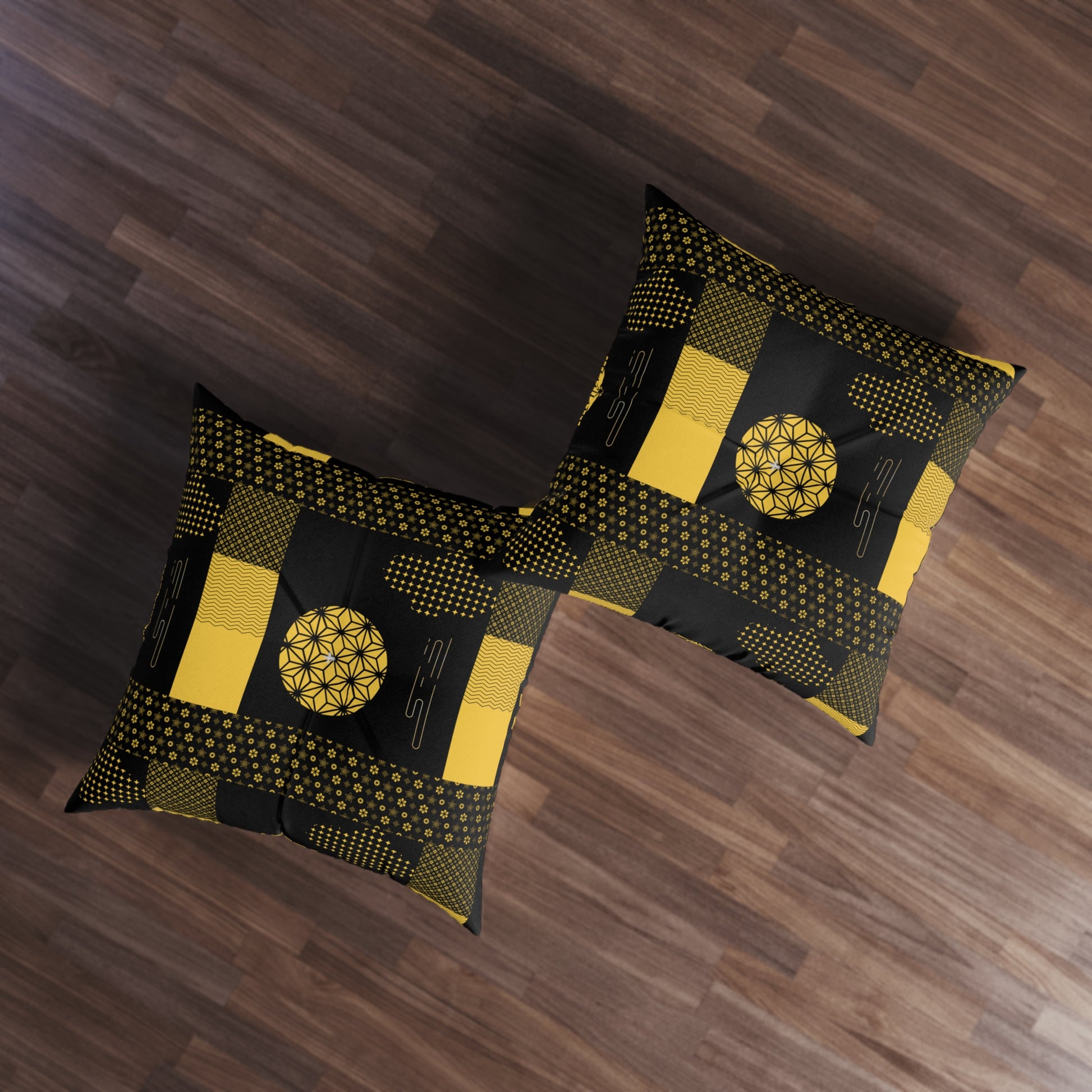 Two square throw pillows with a black and yellow geometric patchwork pattern, displayed on a dark wood floor.
