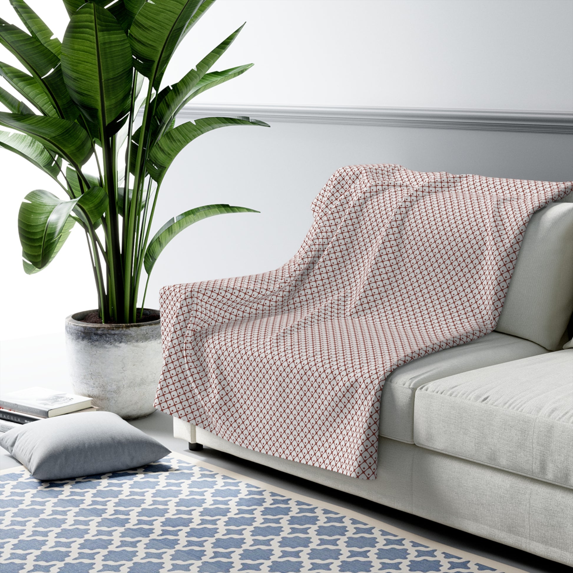 Patterned blanket draped over a sofa in a living room with a plant and rug.