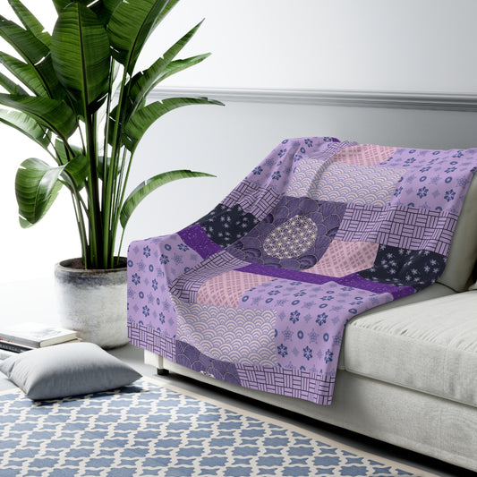 Patchwork blanket with purple and white patterns draped over a sofa in a living room.