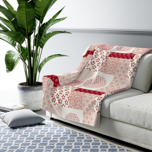 White sofa with a red and white patterned throw blanket, next to a potted plant on a blue patterned rug.
