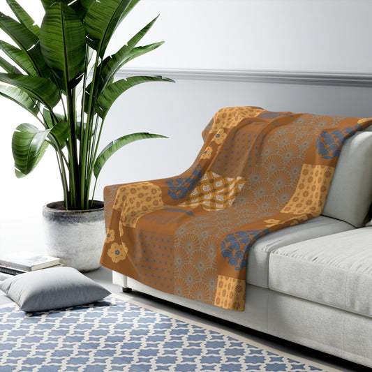 Patterned orange blanket draped over a gray sofa in a living room with a plant and rug.