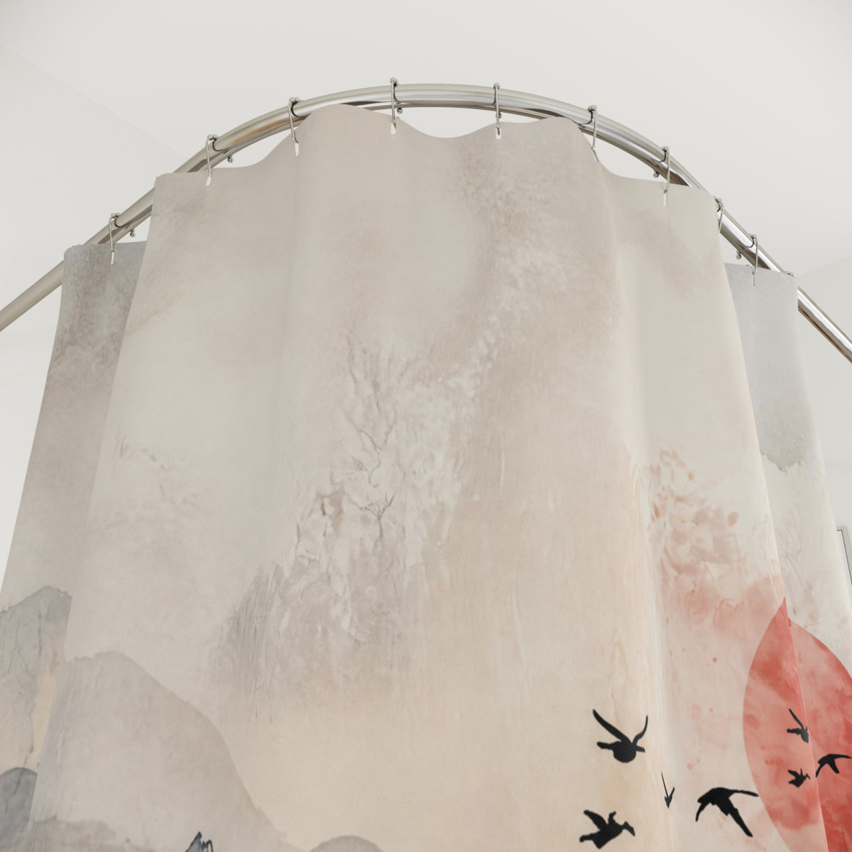 A fabric shower curtain with a minimalist watercolor-style design featuring black birds, gray mountains, and a red sun on an off-white background, hanging from a curved silver metal rod.