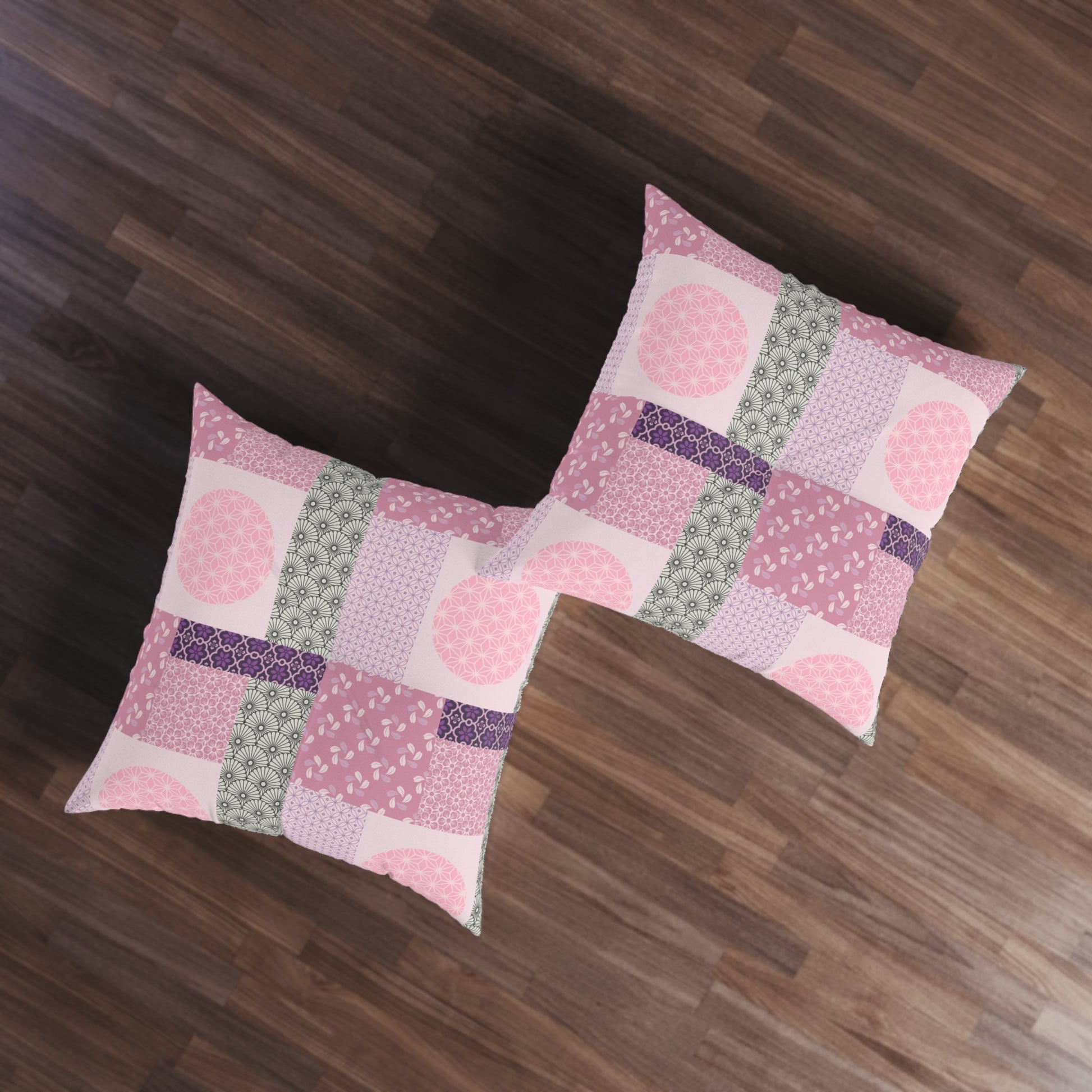Two square patchwork pillows in shades of pink, purple, and sage green, displayed on a dark wood floor.