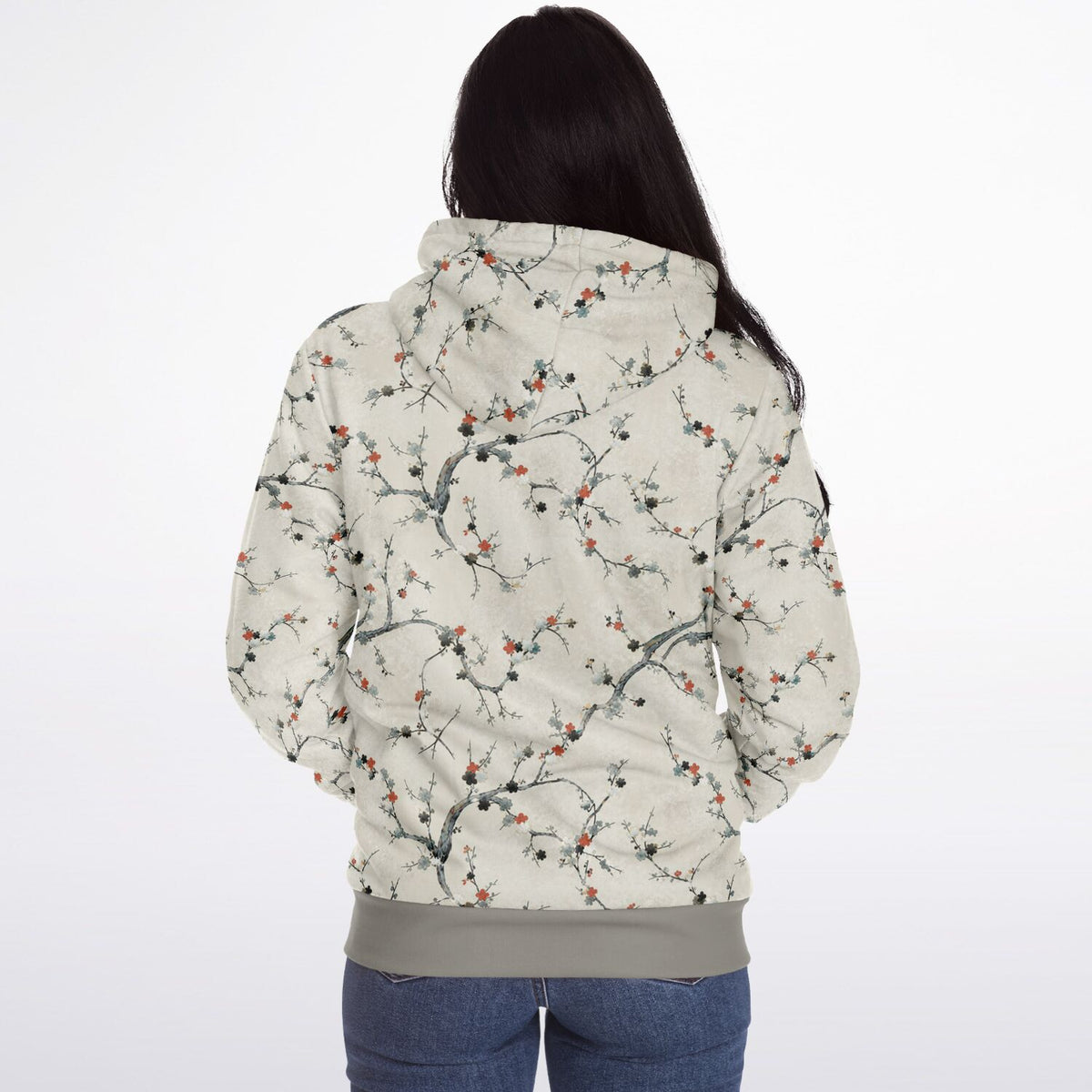 A woman viewed from behind wearing a hooded jacket with an all-over floral branch print on a light beige background, paired with blue jeans, against a plain white studio background.
