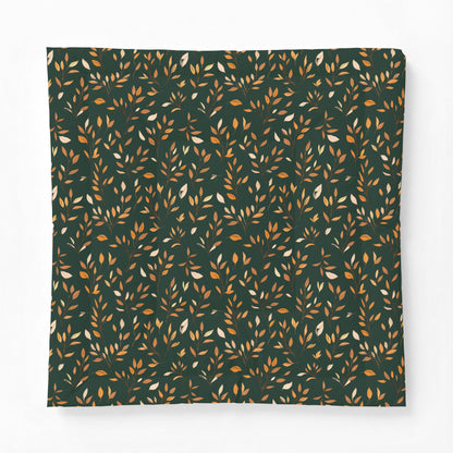 A square fabric item, likely a pillowcase or blanket, featuring an all-over repeating pattern of small leafy branches in warm orange, mustard, and cream on a dark forest green background.