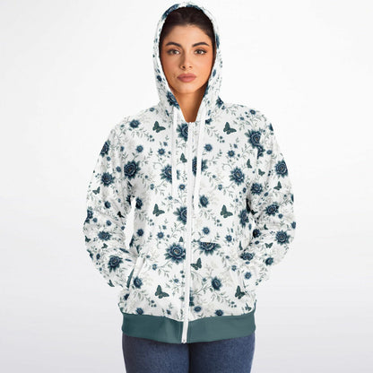 A woman wearing a white zip-up hoodie with a dark teal floral and butterfly pattern, paired with blue jeans, against a plain white background.