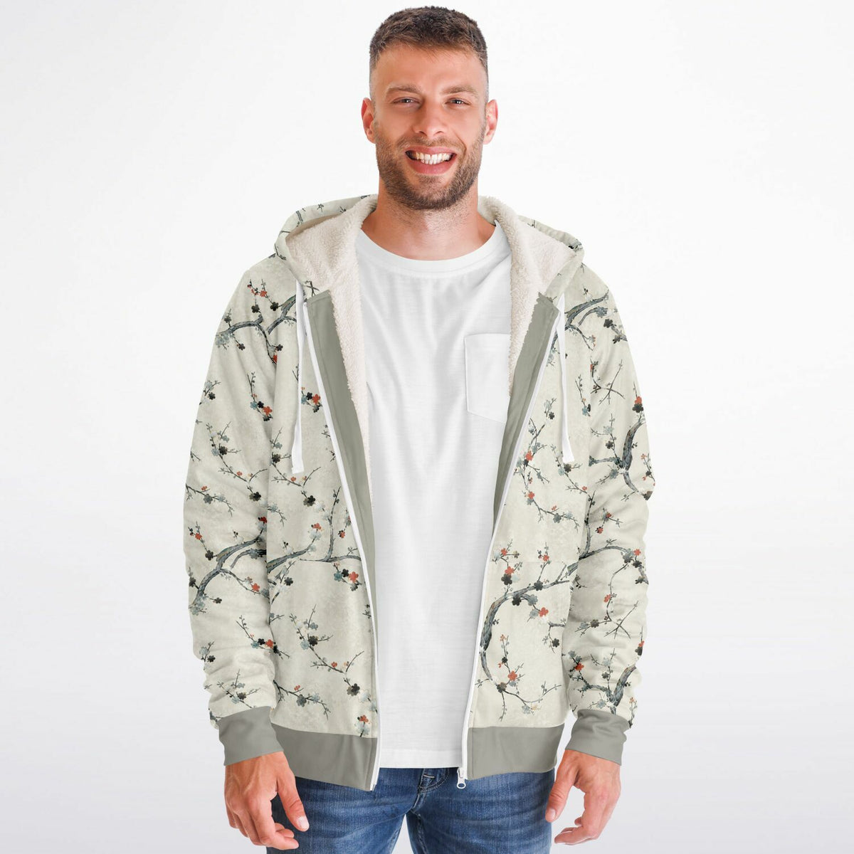 A man wearing a light beige zip-up hoodie with a delicate branch and cherry blossom print, layered over a white t-shirt and blue jeans, against a plain white background.
