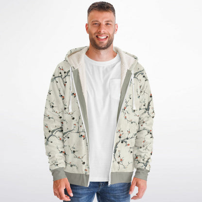 A man wearing a light beige zip-up hoodie with a delicate branch and cherry blossom print, layered over a white t-shirt and blue jeans, against a plain white background.